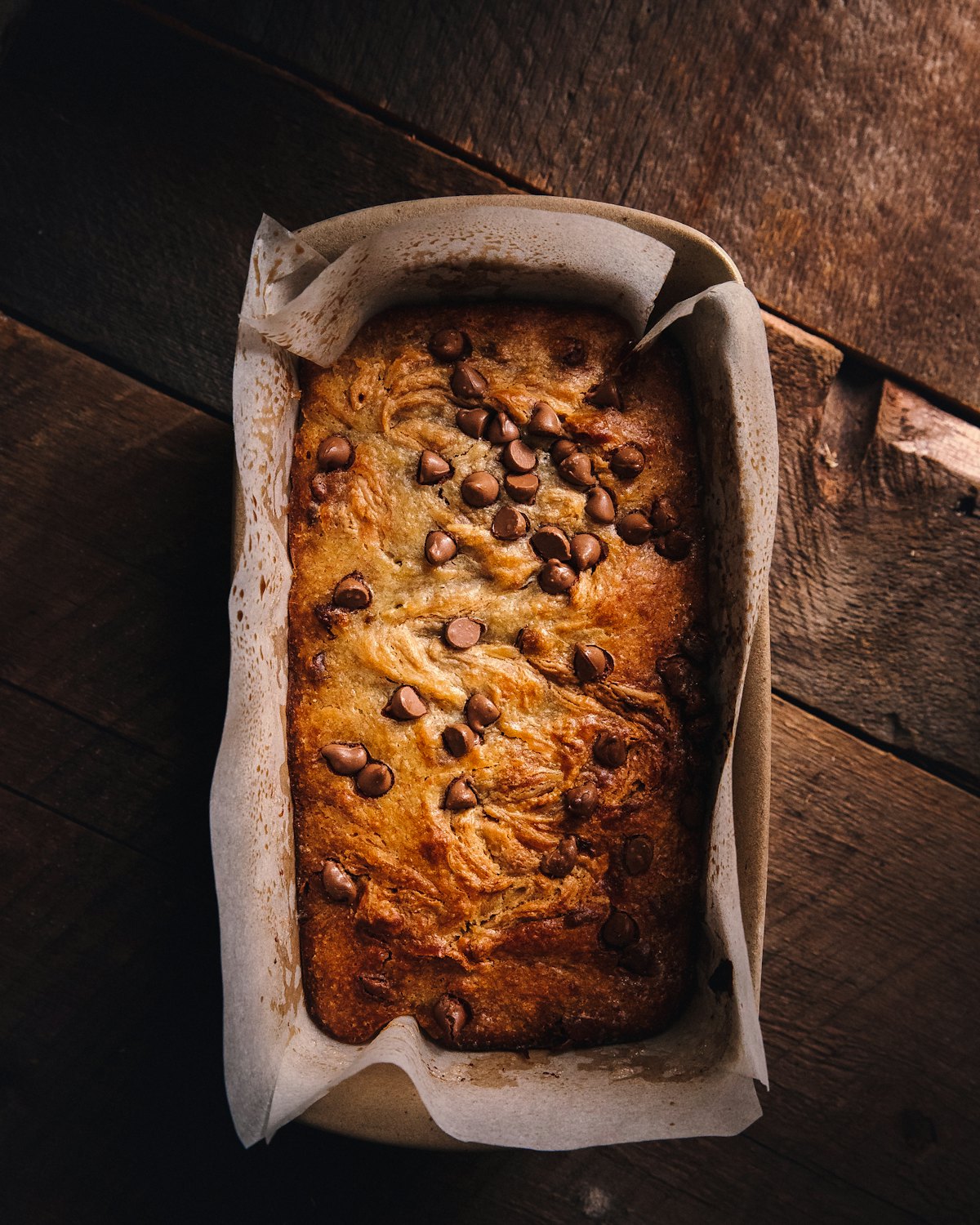 A loaf of banana bread in its tin on dark wood