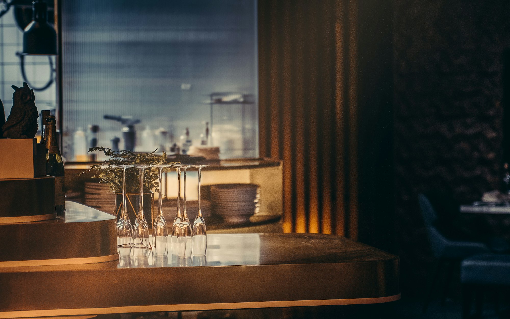 Warm light along a dark bar counter with glassware on the shelf