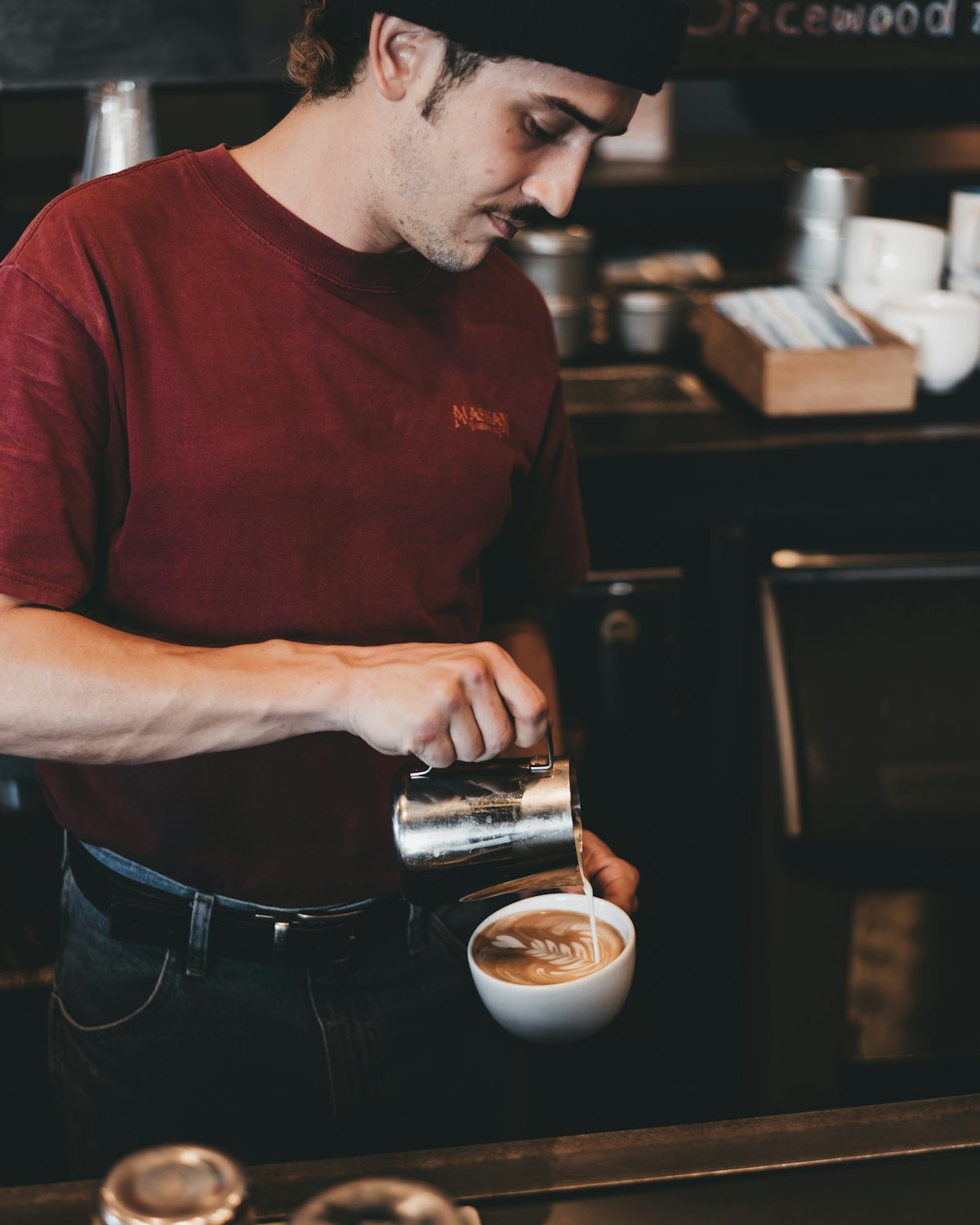 A barista pouring milk into a cup behind a dark counter