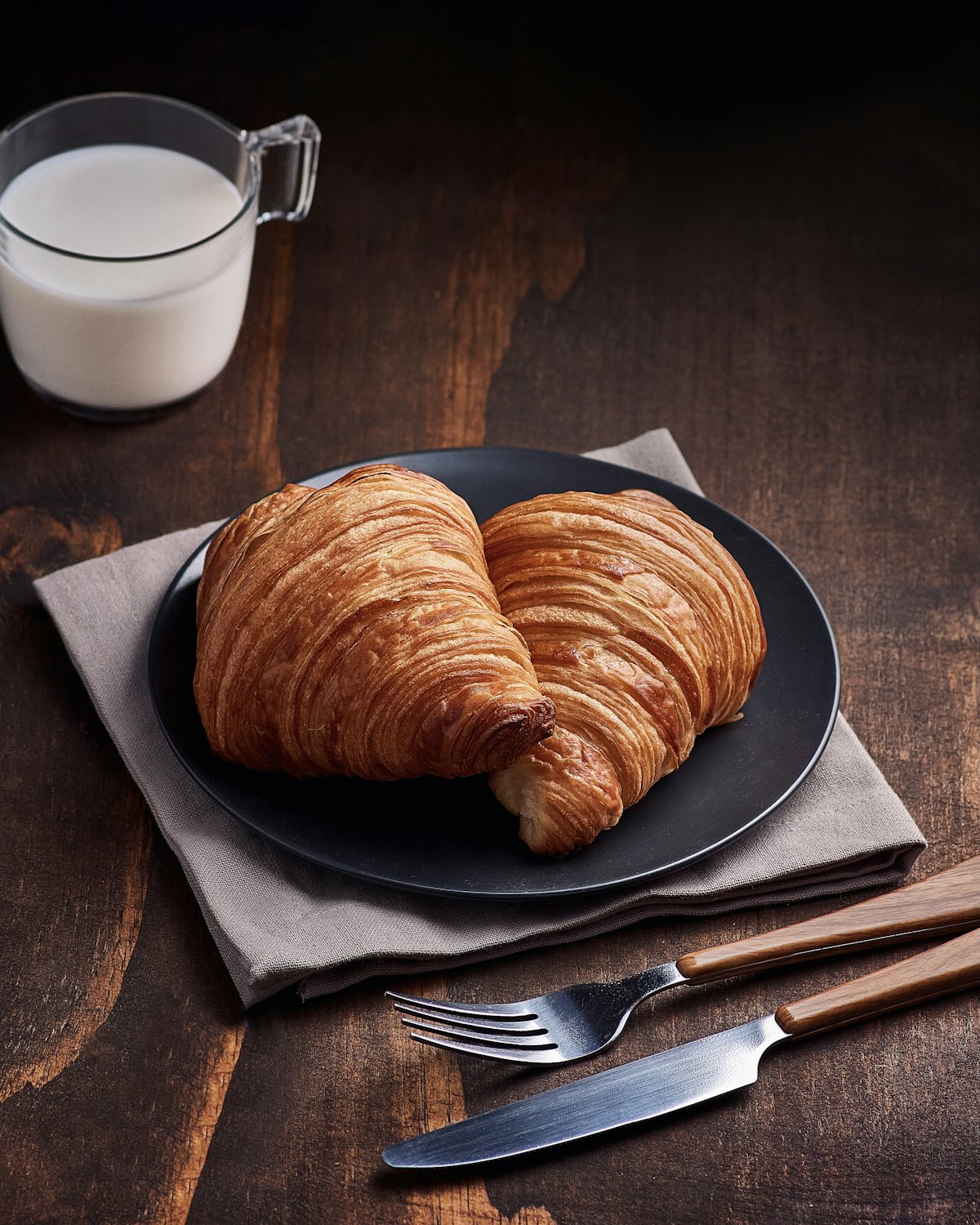 Two croissants on a dark plate on a worn wooden table