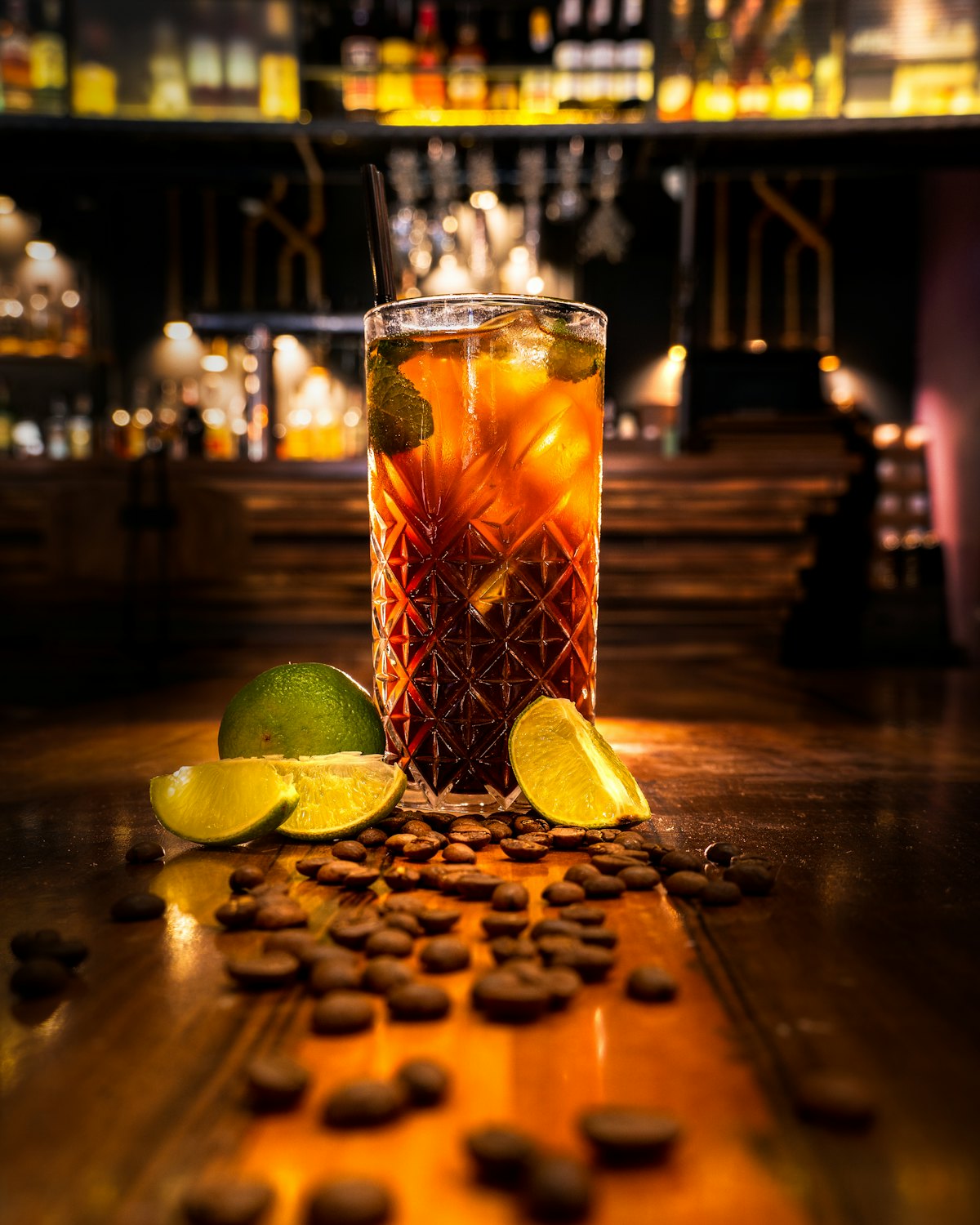 A tall glass of ginger soda with cut limes on a warm wooden bar