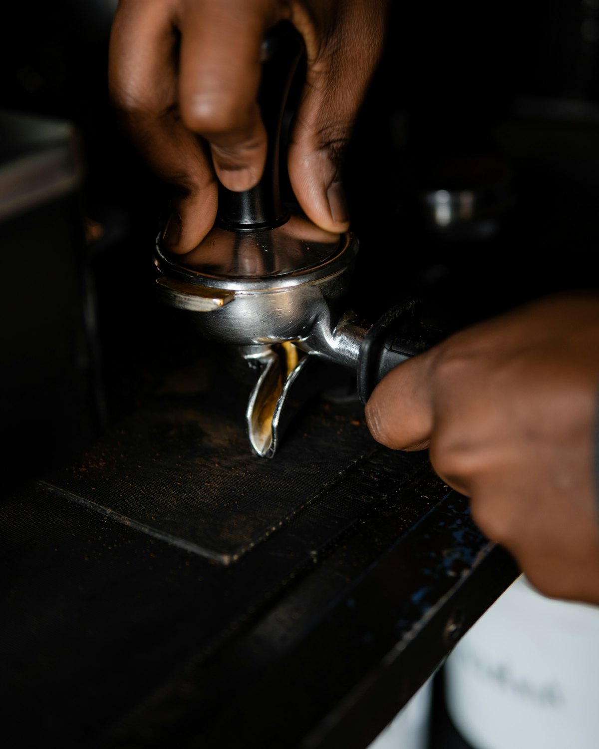Hands tamping ground coffee into a portafilter in low light