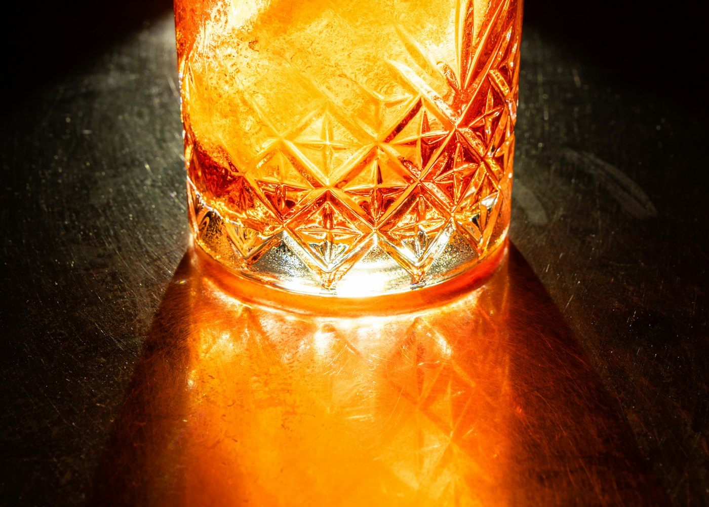 A cut glass of amber tonic lit from below on a dark bar